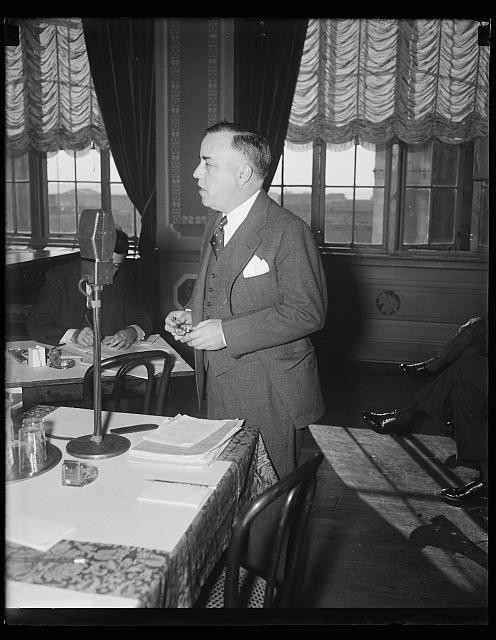Photo:1934 1935 Man Speaking at Microphone in Suited Interior Meeting Room
