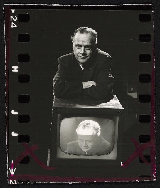 Marshall McLuhan, half-length portrait, standing, leaning on television set on