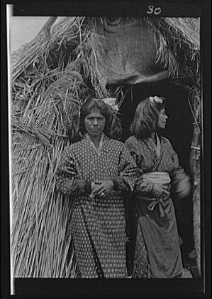 Two Ainu women outside hut entrance,villages,thatched structures,A Genthe,1908