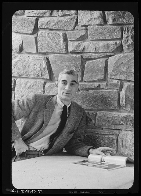 Charles M. Goodman, portrait in front of stone chimney in living room at his