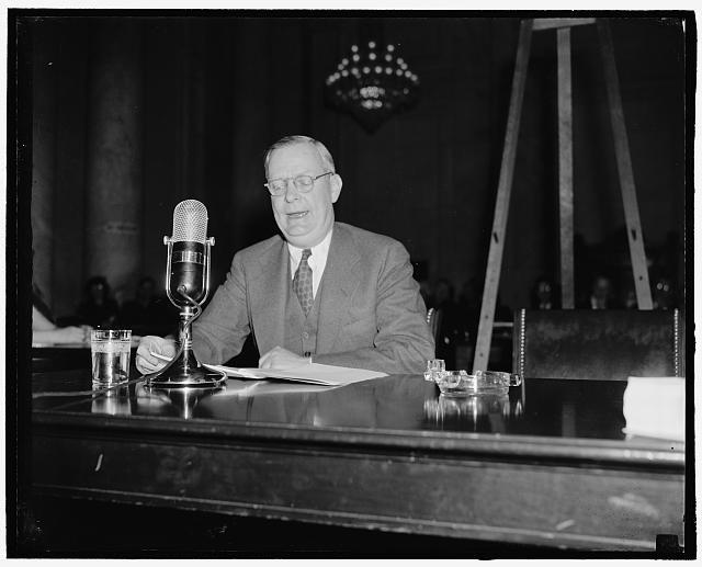 Photo:1940s Man at Microphone Speaking at Desk Press Conference