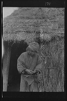 Ainu woman outside entrance,hut,villages,thatched buildings,Arnold Genthe,1908